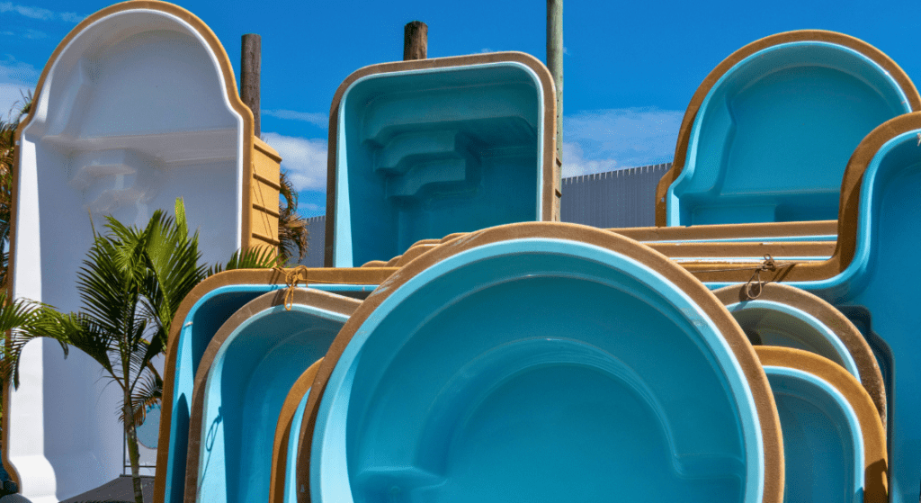 A stack of fiberglass pool shells is displayed outdoors with palm trees and a blue sky in the background. Fiber Glass Pool Shell 