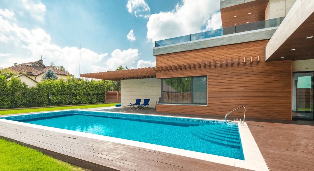 Modern house with a wooden facade and a swimming pool. Two blue lounge chairs are on the poolside deck, and a green hedge lines the property. Your Dream Pool & Spa with Sutton Pools in Sango, TN