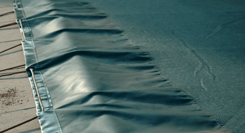 Close-up of a blue protective cover stretched over an outdoor pool, with a portion of the pool deck visible on the side.