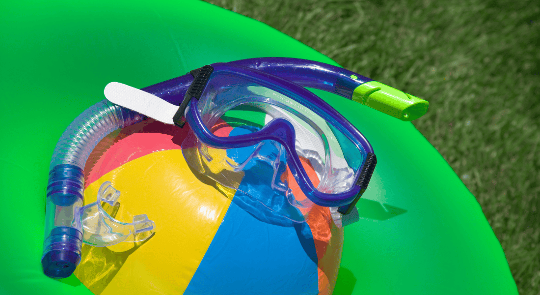A colorful beach ball with a snorkel mask and tube is placed on a green inflatable in a grassy area.